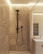 A modern bathroom interior featuring a shower area with intricately patterned tiles in earthy tones. The showerhead and fittings are matte black, adding a contemporary flair. Adjacent to the shower is a vanity with a mirrored section, a sink, and small toiletries placed on the counter. Soft ambient lighting adds a cozy atmosphere to the space.