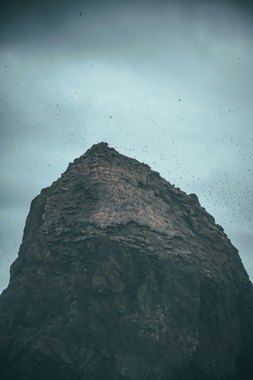 a very tall rock with a bunch of birds flying around it