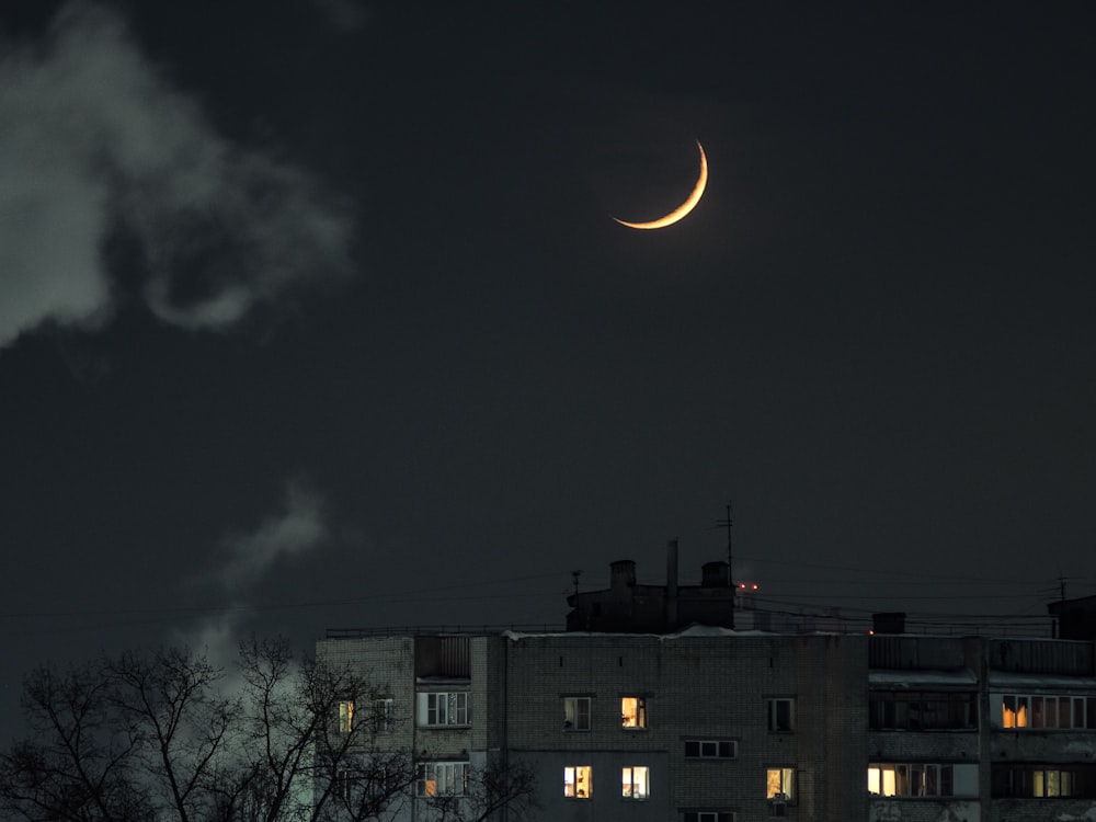 uma lua crescente é vista no céu noturno sobre um edifício