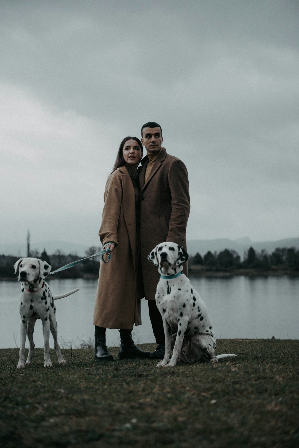 a man and woman standing next to two dalmatian dogs