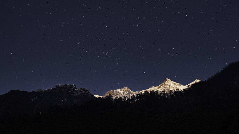 the night sky with stars above a mountain range