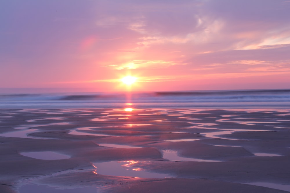 the sun is setting over the water on the beach