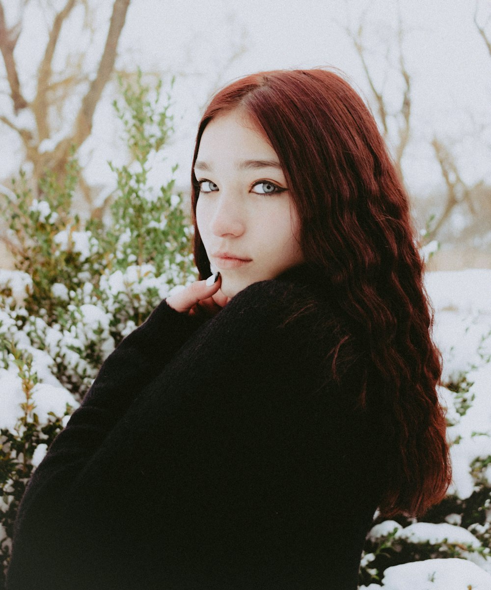 a woman with long red hair standing in the snow