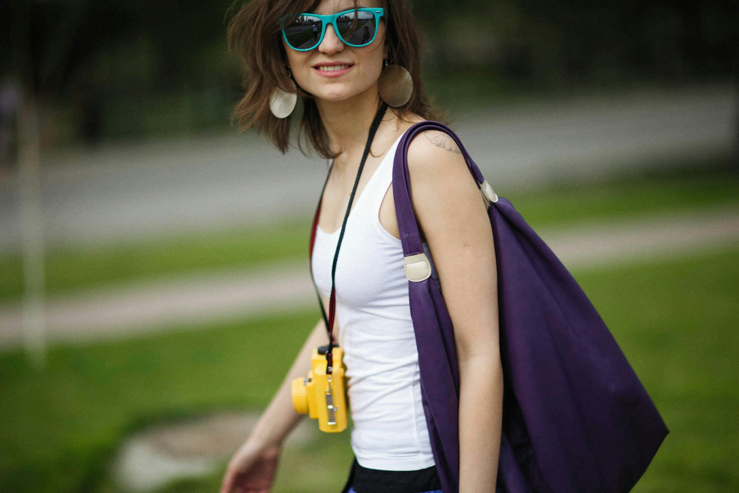 a woman wearing sunglasses and carrying a purple bag