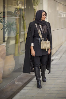 a woman walking down a sidewalk wearing a black coat