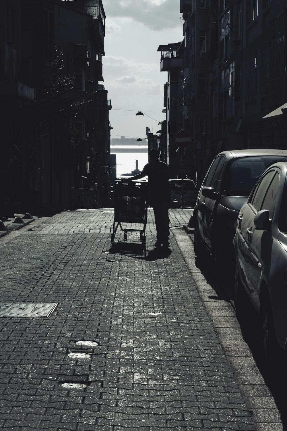 a man pushing a cart down a street next to parked cars