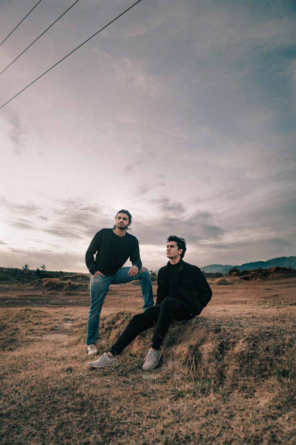 a couple of men sitting on top of a dry grass field