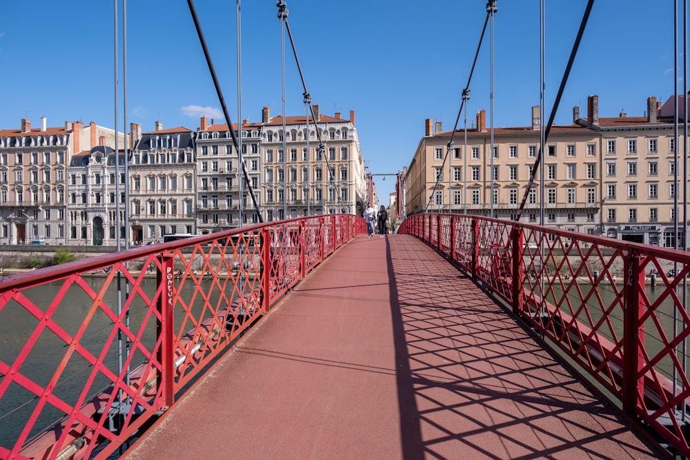 a red pedestrian bridge over a river with buildings in the background