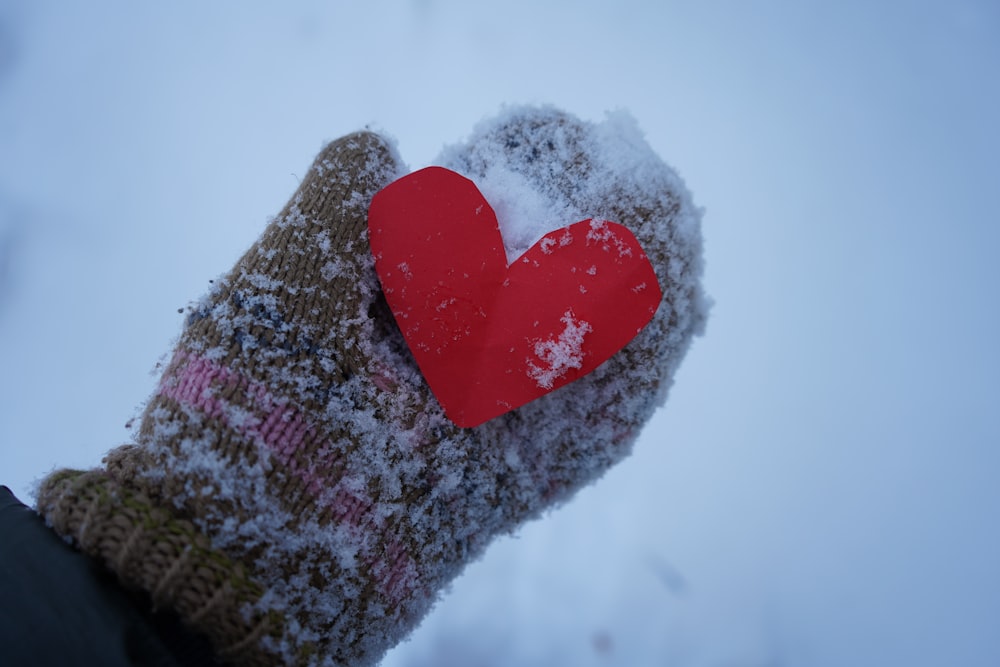 a hand holding a red heart in the snow