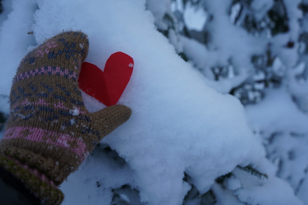 a gloved hand holding a red heart in the snow