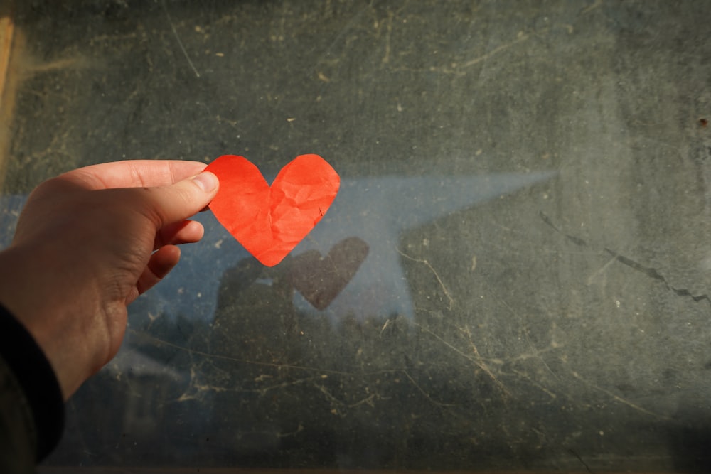 a hand holding a piece of paper with a heart cut out of it