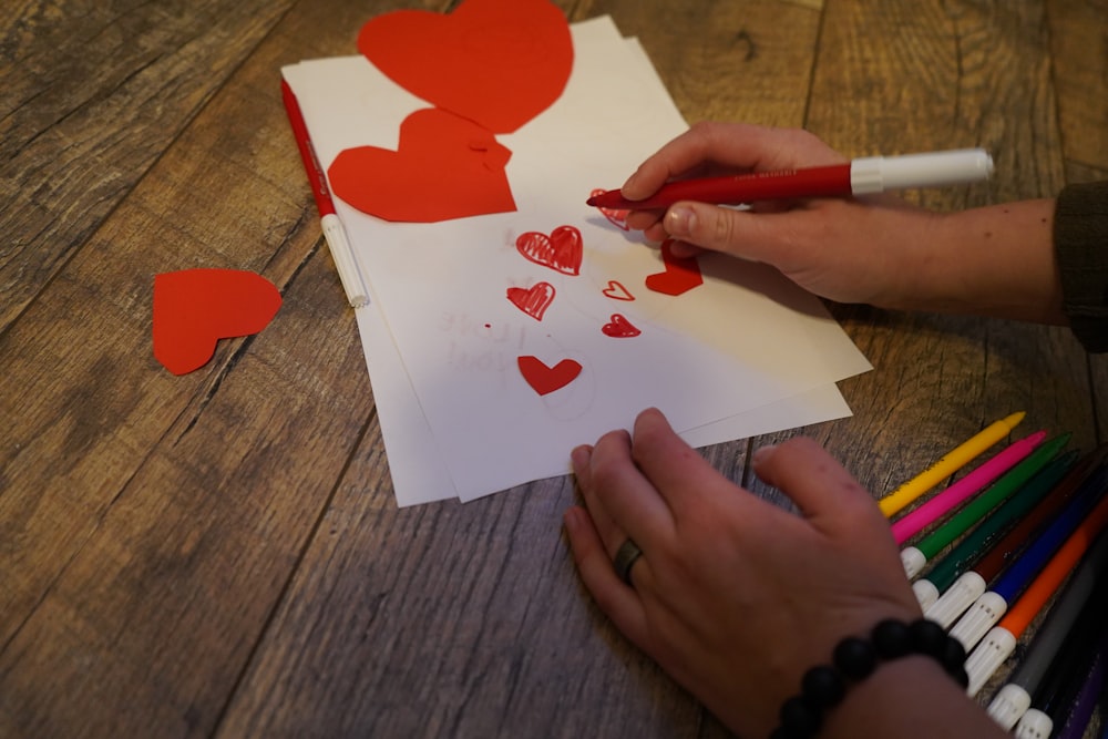 Eine Person schneidet Herzen auf einem Blatt Papier aus