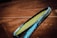 A close-up of a tennis racket with a blue frame and yellow strings, held against the blurred background of a clay tennis court.