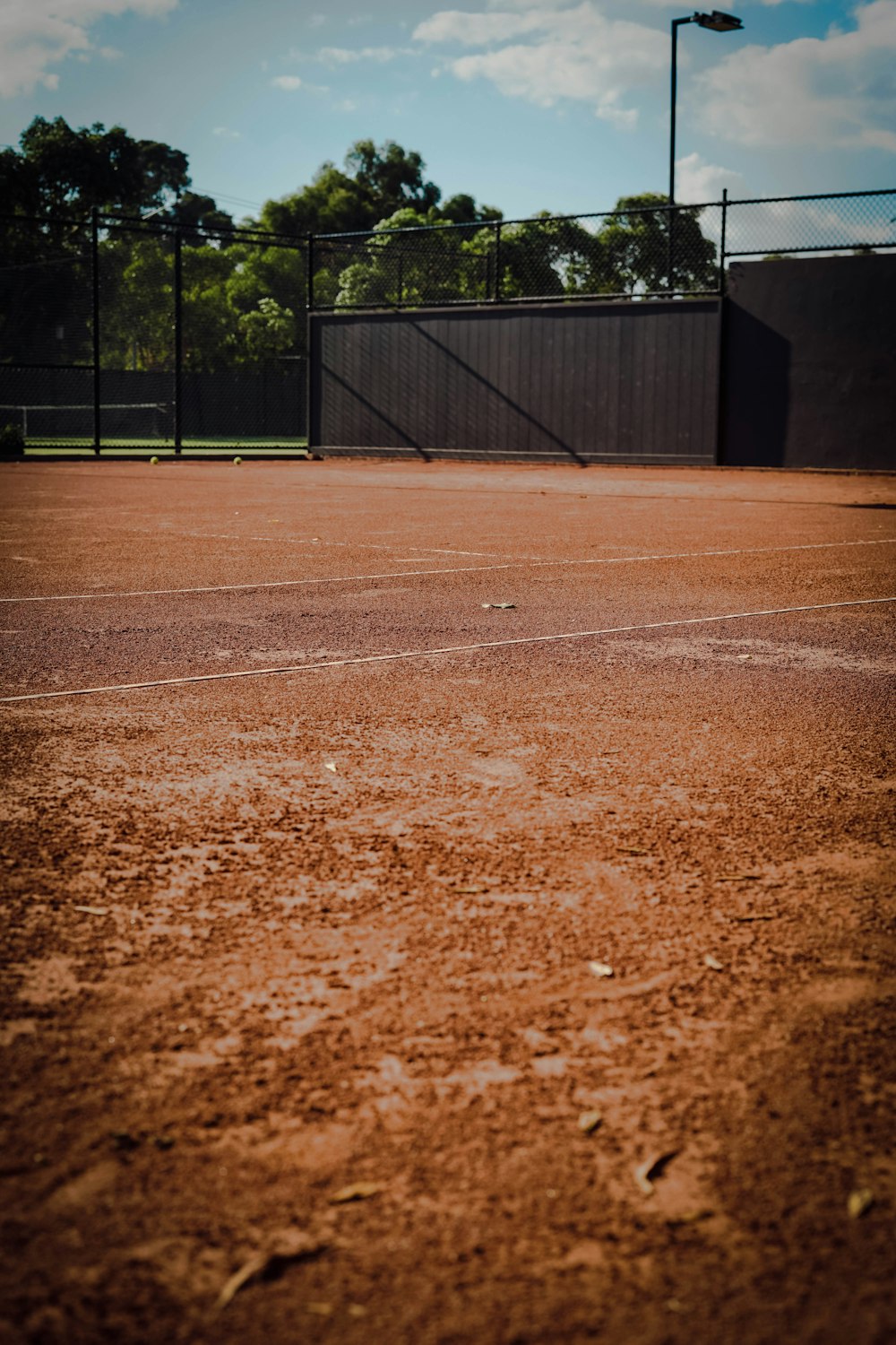 a dirt tennis court with a fence in the background