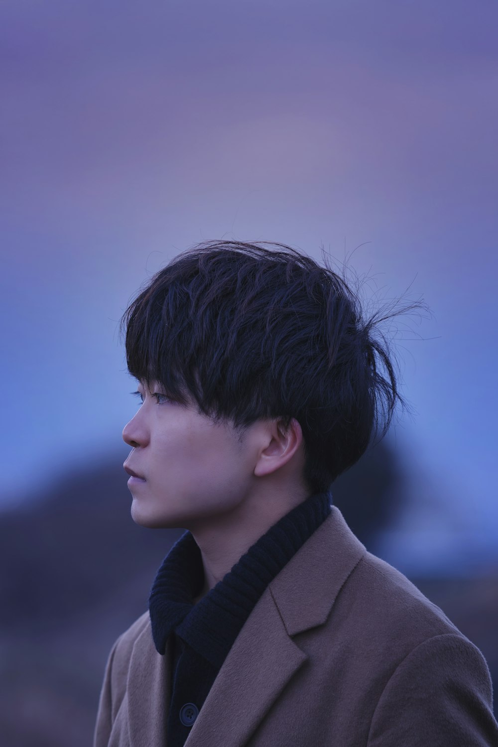 a man with black hair standing in front of a blue sky