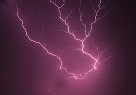 Bright pink lightning bolts sharply illuminate the dark background, creating an electrifying and dramatic visual effect.