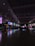 An expansive indoor space with high ceilings and numerous illuminated digital screens displaying various advertisements and information. The polished floor reflects the colorful lights, and the area appears spacious and quiet.