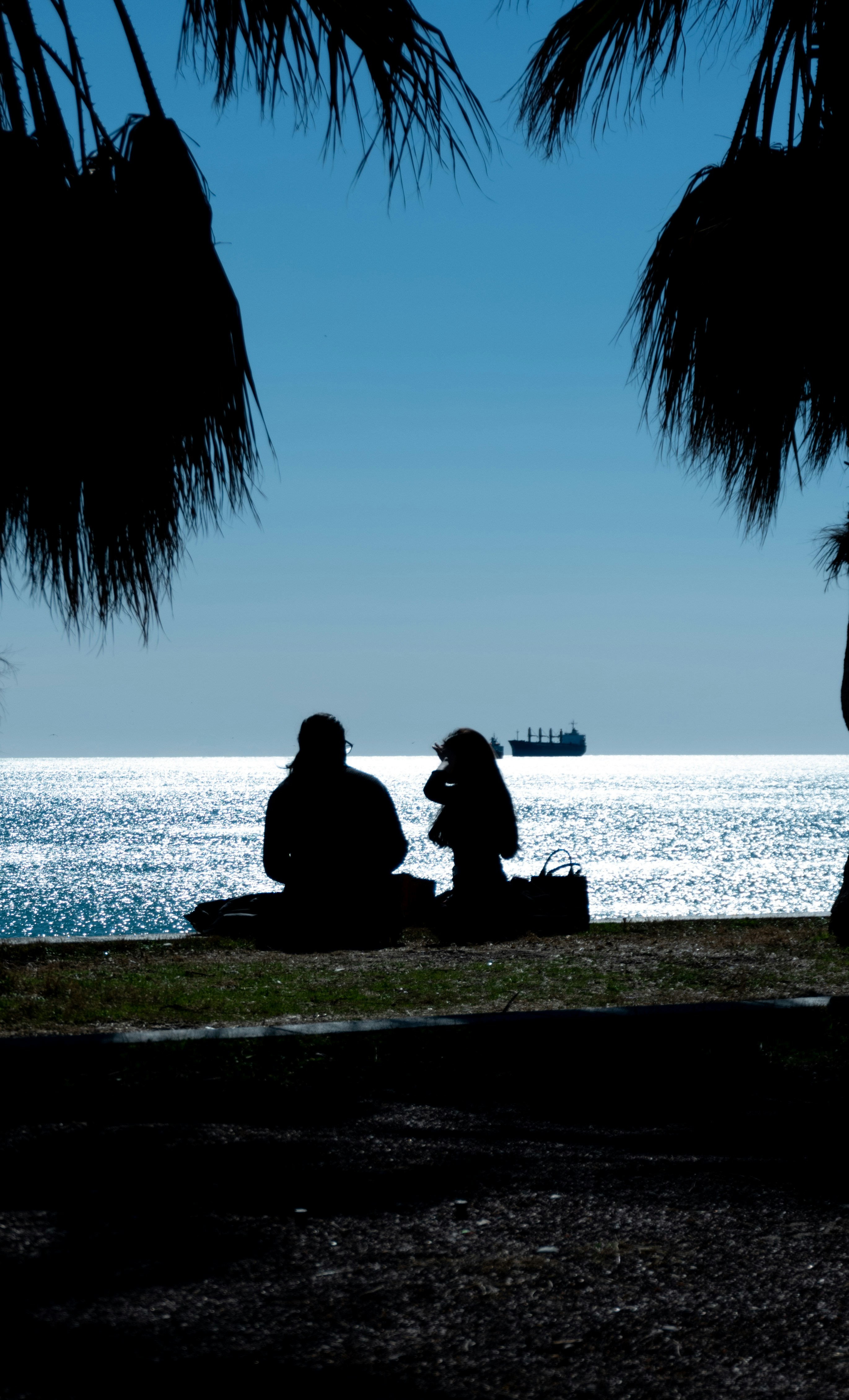 A couple of people sitting next to a body of water photo – Free Tree ...