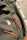 Close-up of a colorful kawaii enamel pin on a backpack strap with soft pastel background.