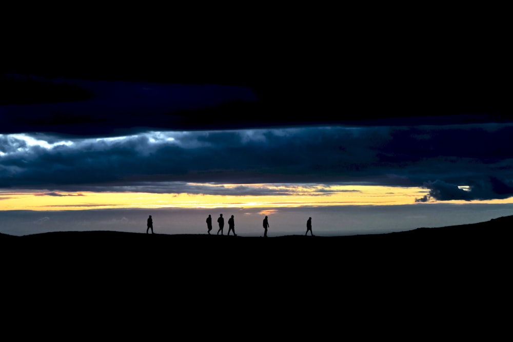 a group of people standing on top of a hill under a cloudy sky