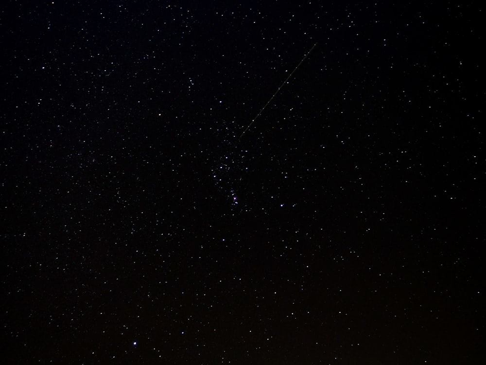 a night sky with stars and a plane in the distance