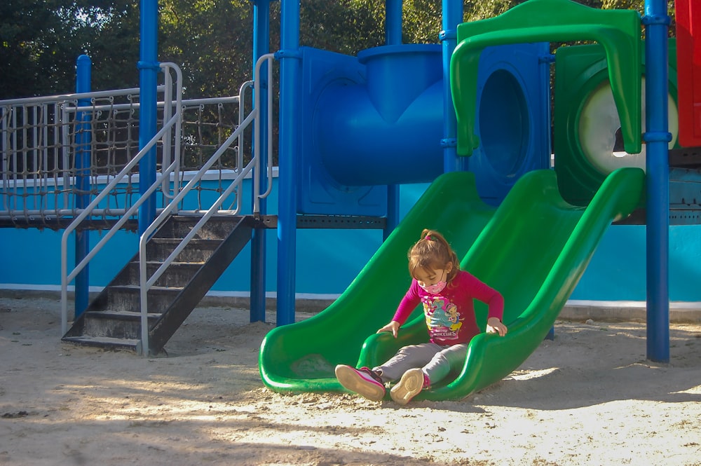 a little girl sitting on a slide in a playground