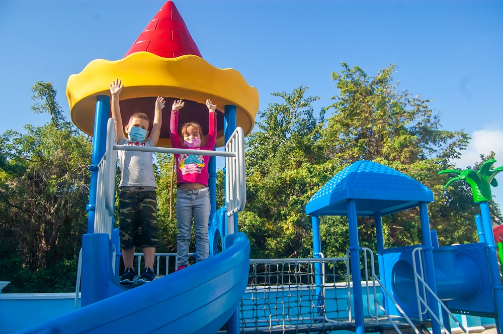 a couple of kids standing on top of a slide