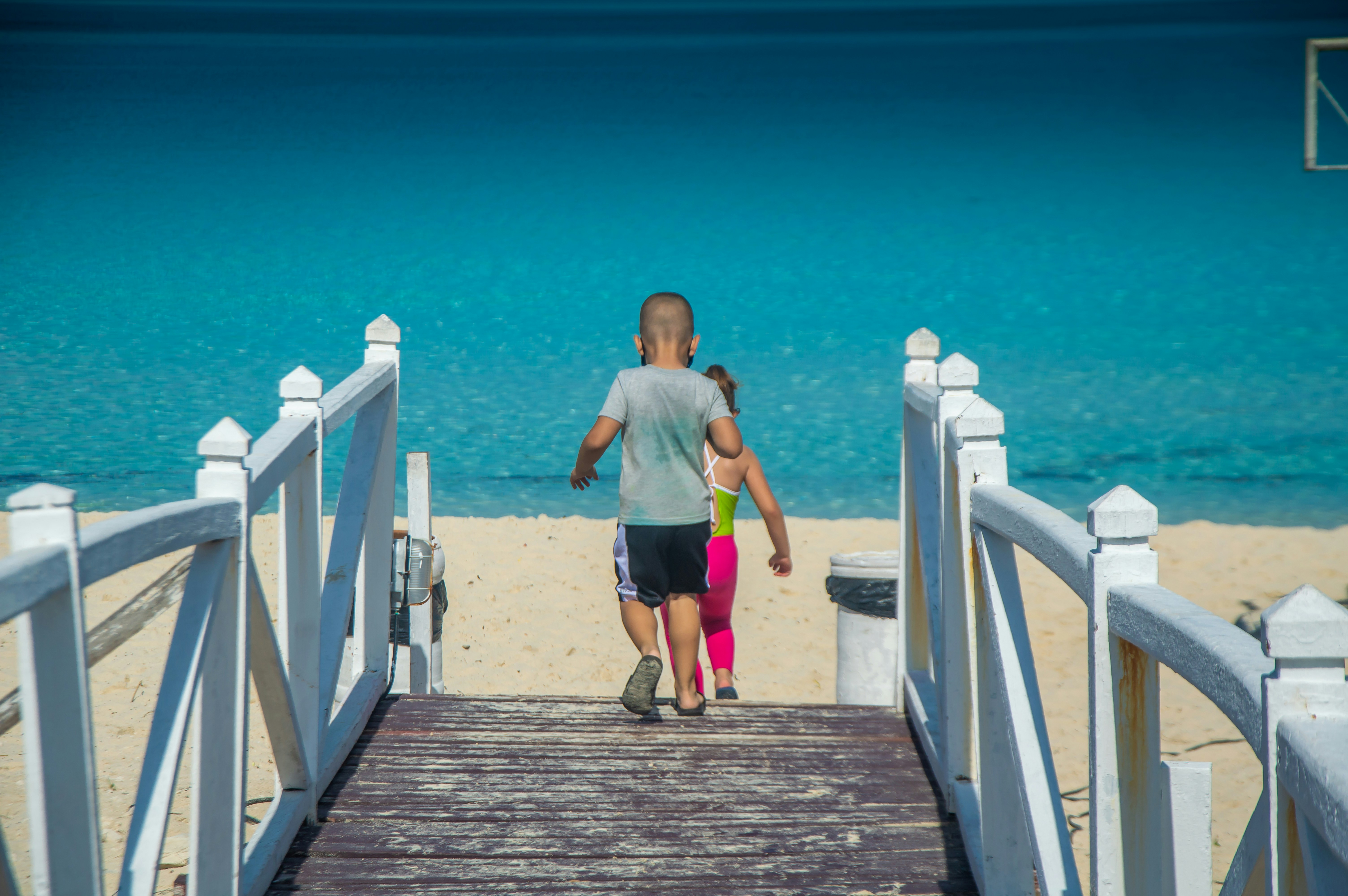 a man and a little girl walking down a pier, Two children arriving at the beach through the walkway