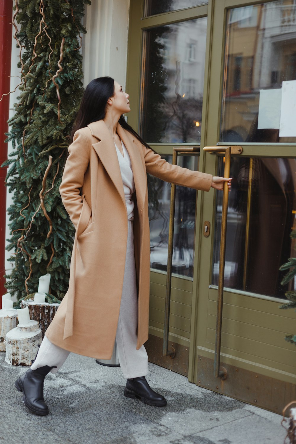 a woman in a tan coat is standing outside of a building