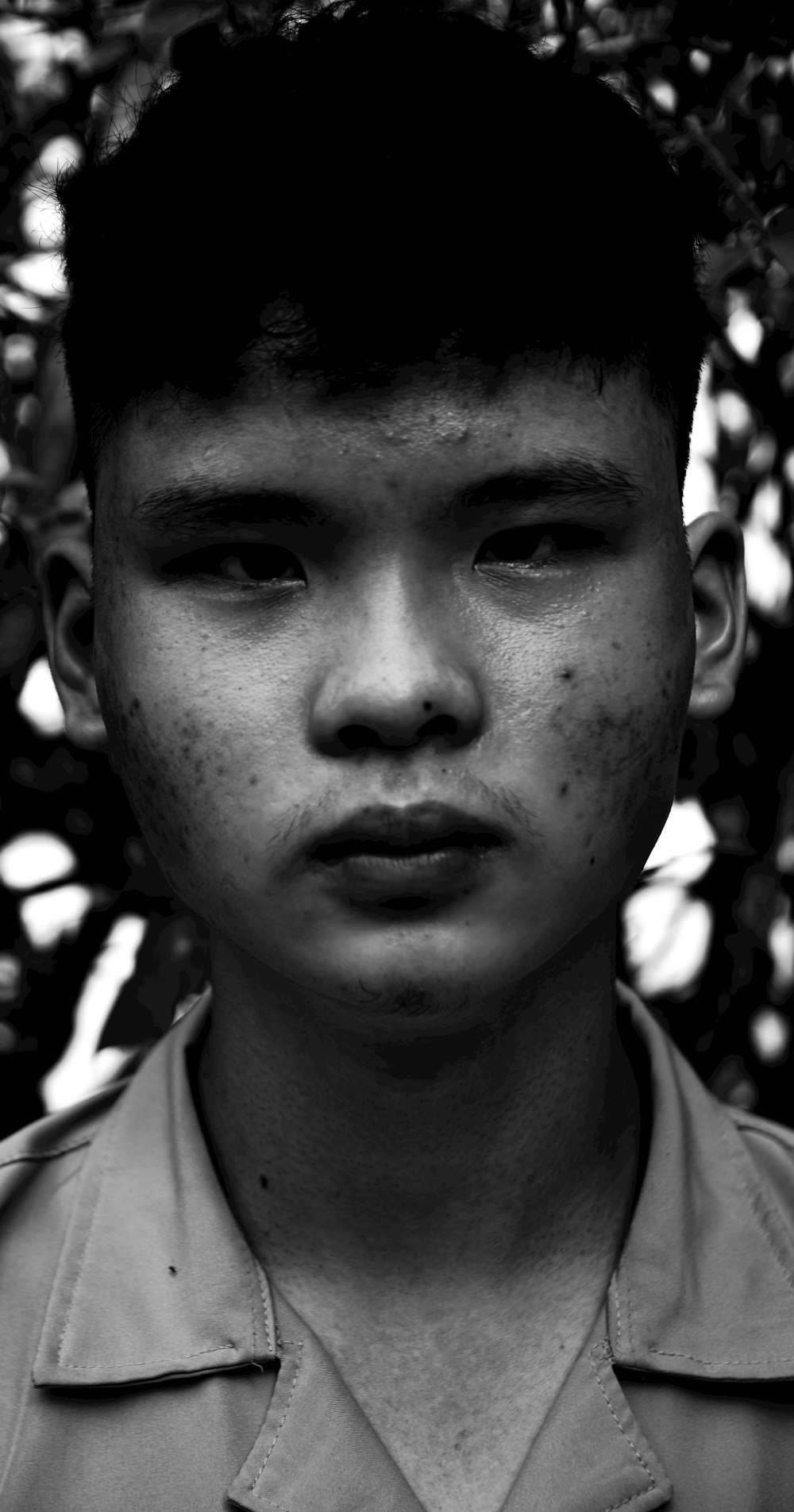 a young man in a uniform standing in front of a bush