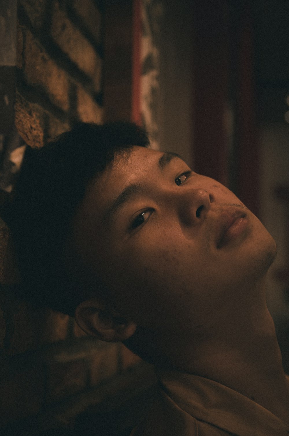 a young man leaning against a brick wall