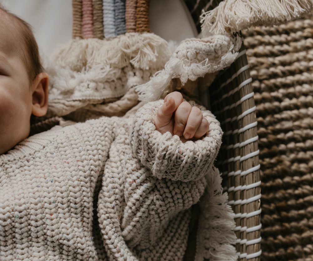 a baby in a sweater laying on a wicker chair
