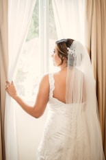 a woman in a wedding dress looking out a window