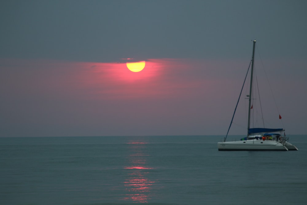 the sun is setting over the ocean with a sailboat in the foreground