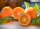Fresh oranges are displayed on a light wooden surface, with one orange cut in half to reveal its juicy interior. Green leaves are attached to the oranges, adding a natural and vibrant touch.