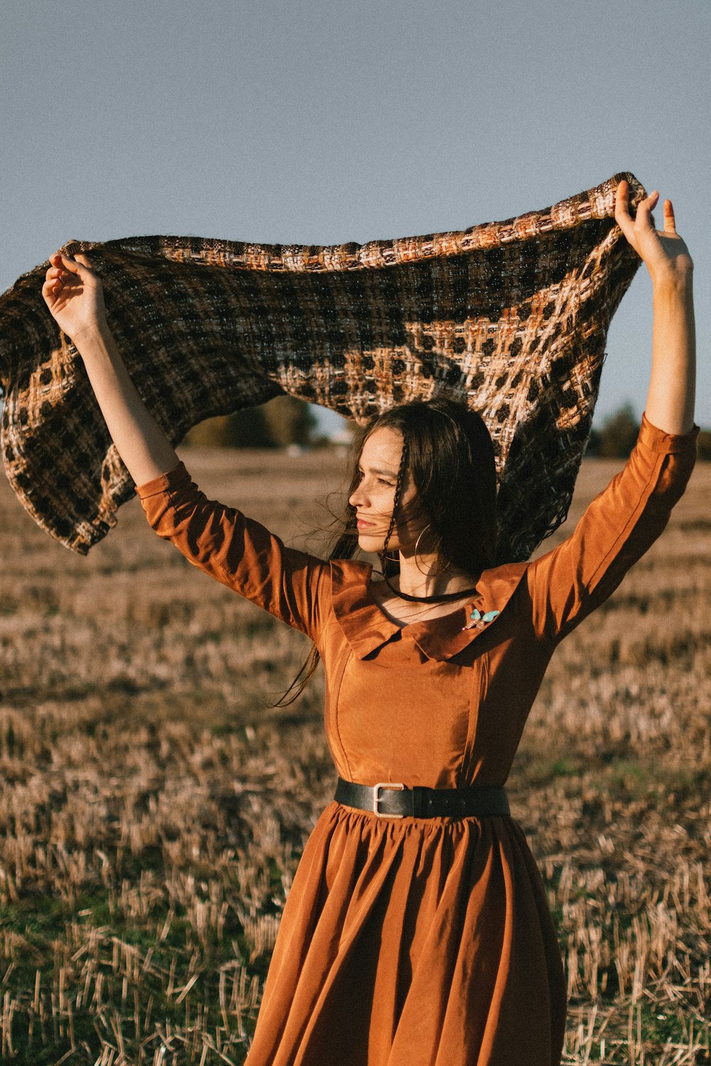 a woman in an orange dress holding a plaid blanket over her head