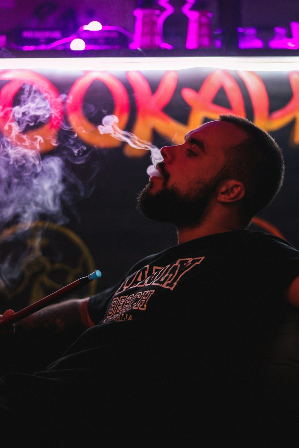 a man smoking a cigarette in front of a neon sign