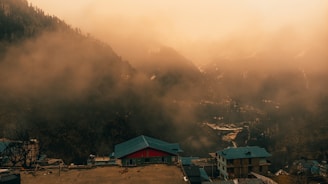A misty mountain village at dawn with soft light illuminating traditional rooftops