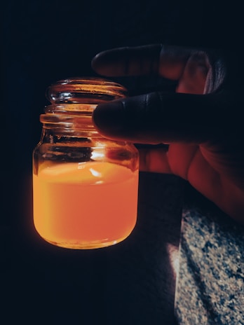 A hand holding a small jar of herbal tincture with natural sunlight streaming in the background.