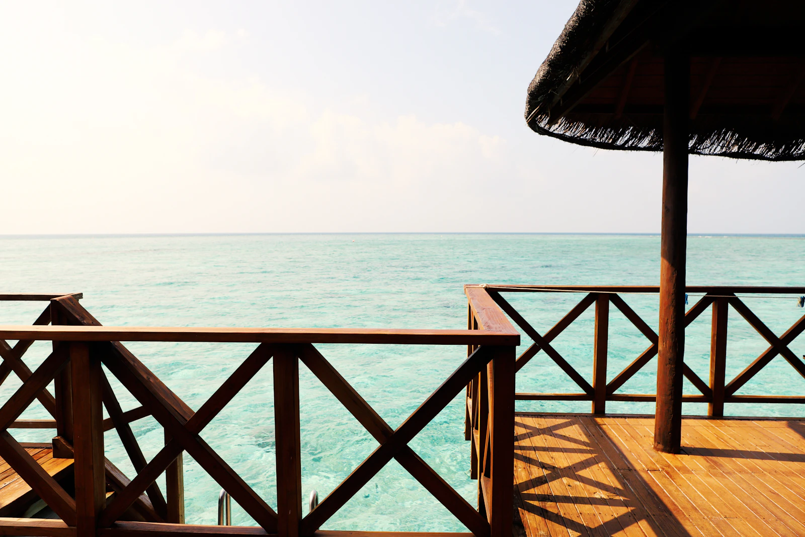 Private overwater villa terrace with wooden deck, thatched roof, and direct ladder access to a turquoise lagoon