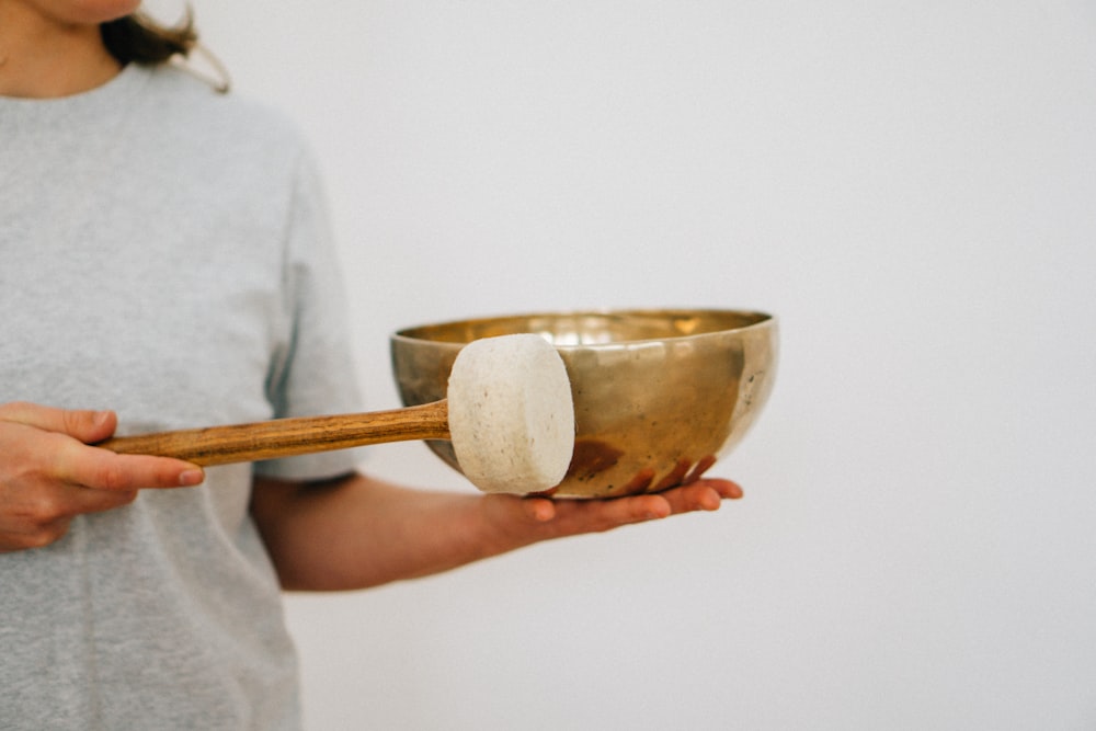 a woman holding a metal bowl with a wooden spoon