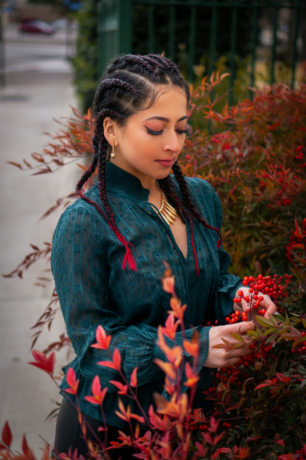 a woman standing in front of a bush with red flowers