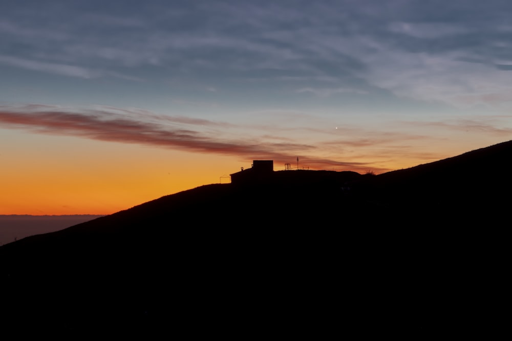 the sun is setting over a hill with a building on it