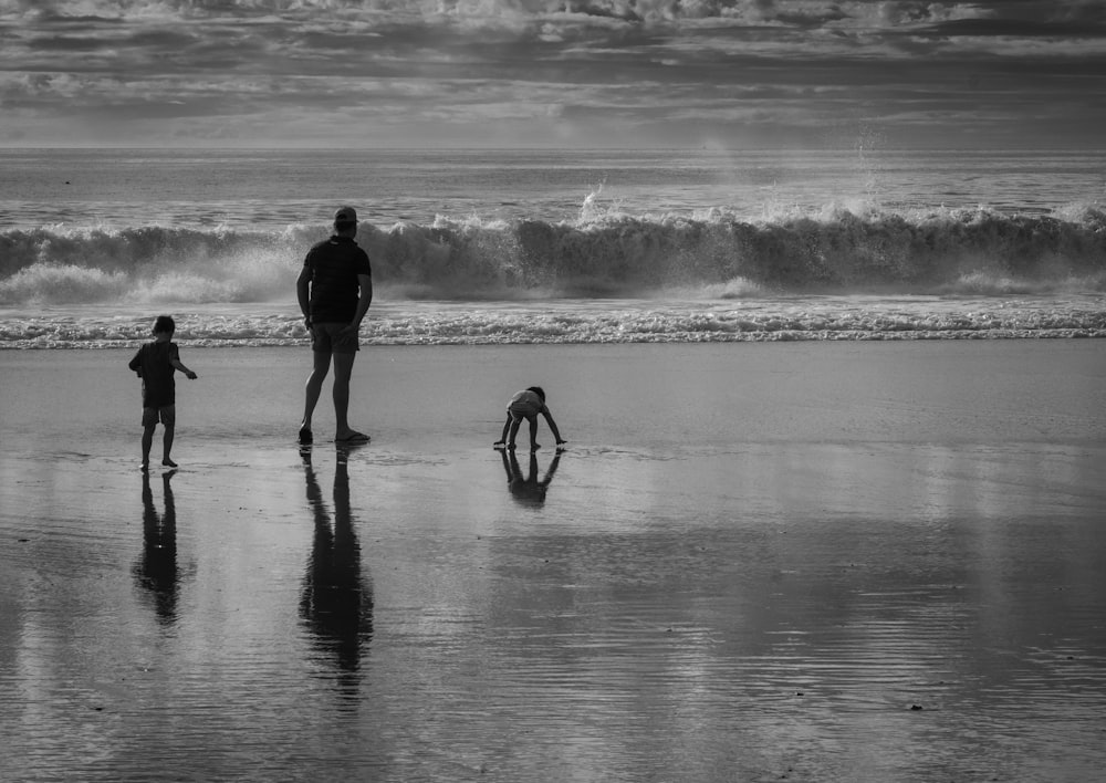 a black and white photo of three people on the beach