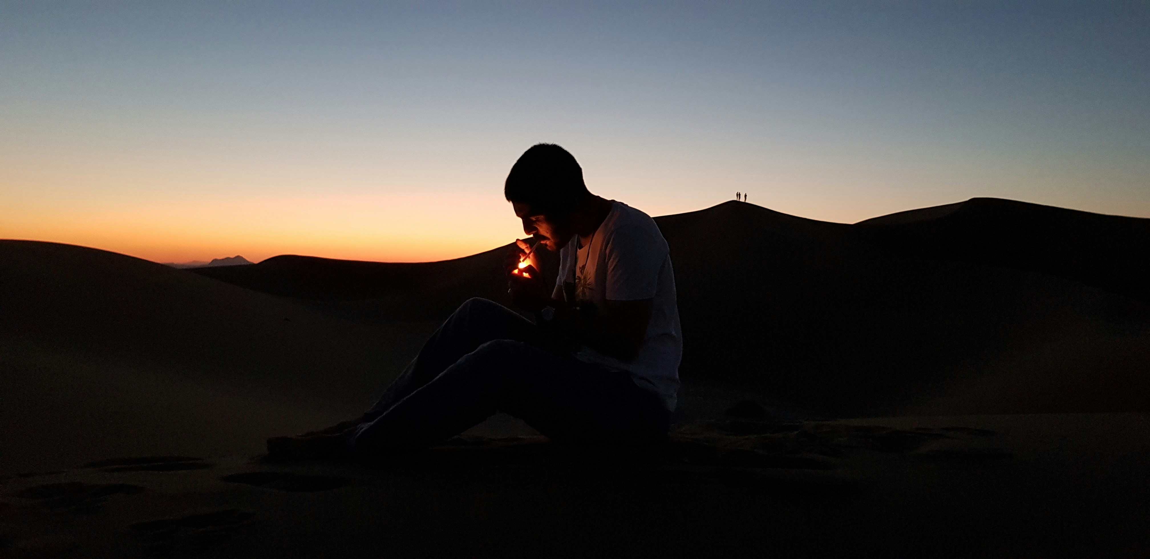 a man sitting on top of a sand dune