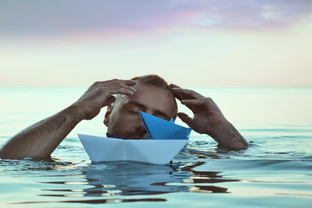 a man is floating in the water with a paper boat