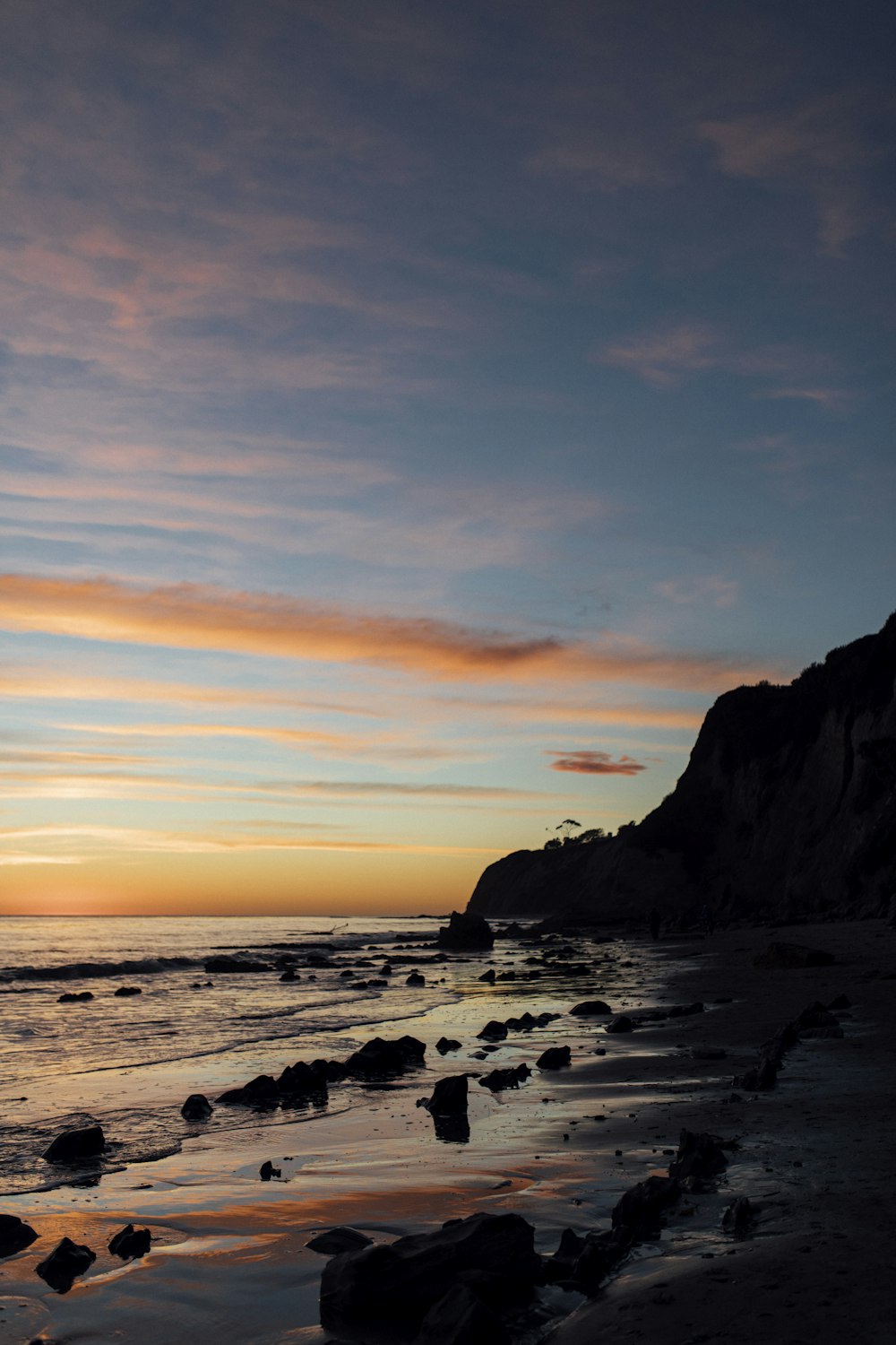 El sol se está poniendo sobre el océano con rocas en primer plano