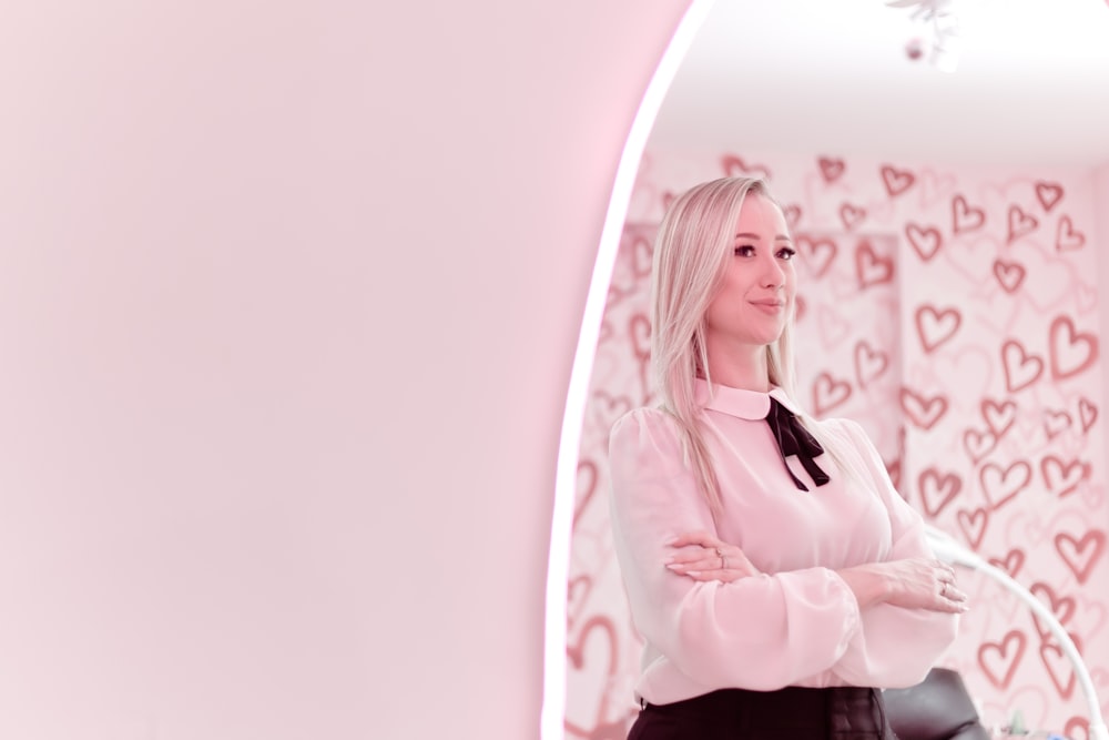 a woman standing in front of a pink wall with hearts on it