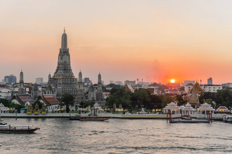 Wat Arun temple on the Chao Phraya River in Bangkok at sunset with river boats in the foreground