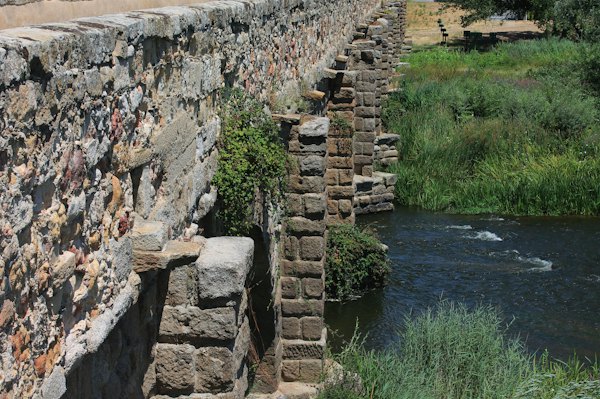 A stone bridge over a river next to a lush green field — Kuldīga, Latvia